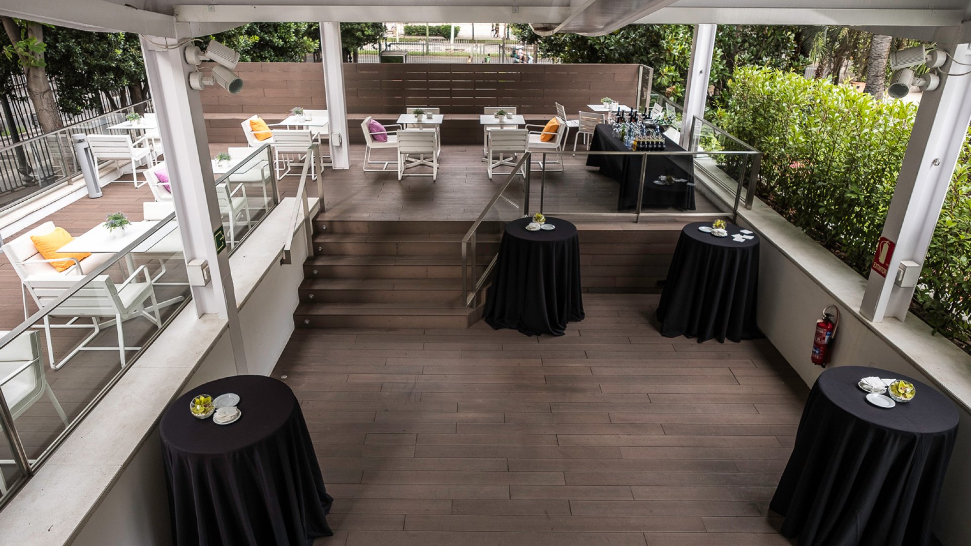 Terraza con suelo de madera oscura y mesas redondas vestidas con manteles negros a los lados