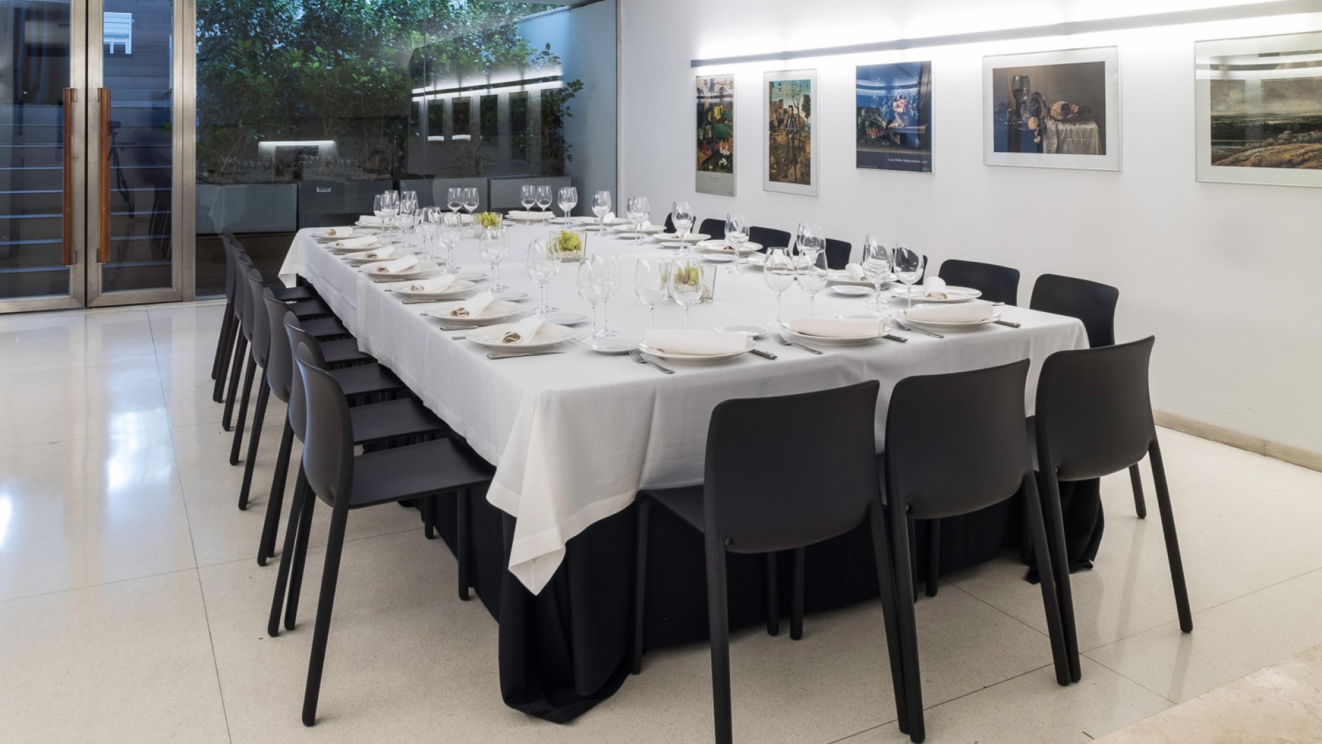 Sala con una cristalera que sale a la terraza, en el centro de la sala hay una mesa rectangular preparada para que se celebre una comida, en la pared hay cuadros famosos del museo