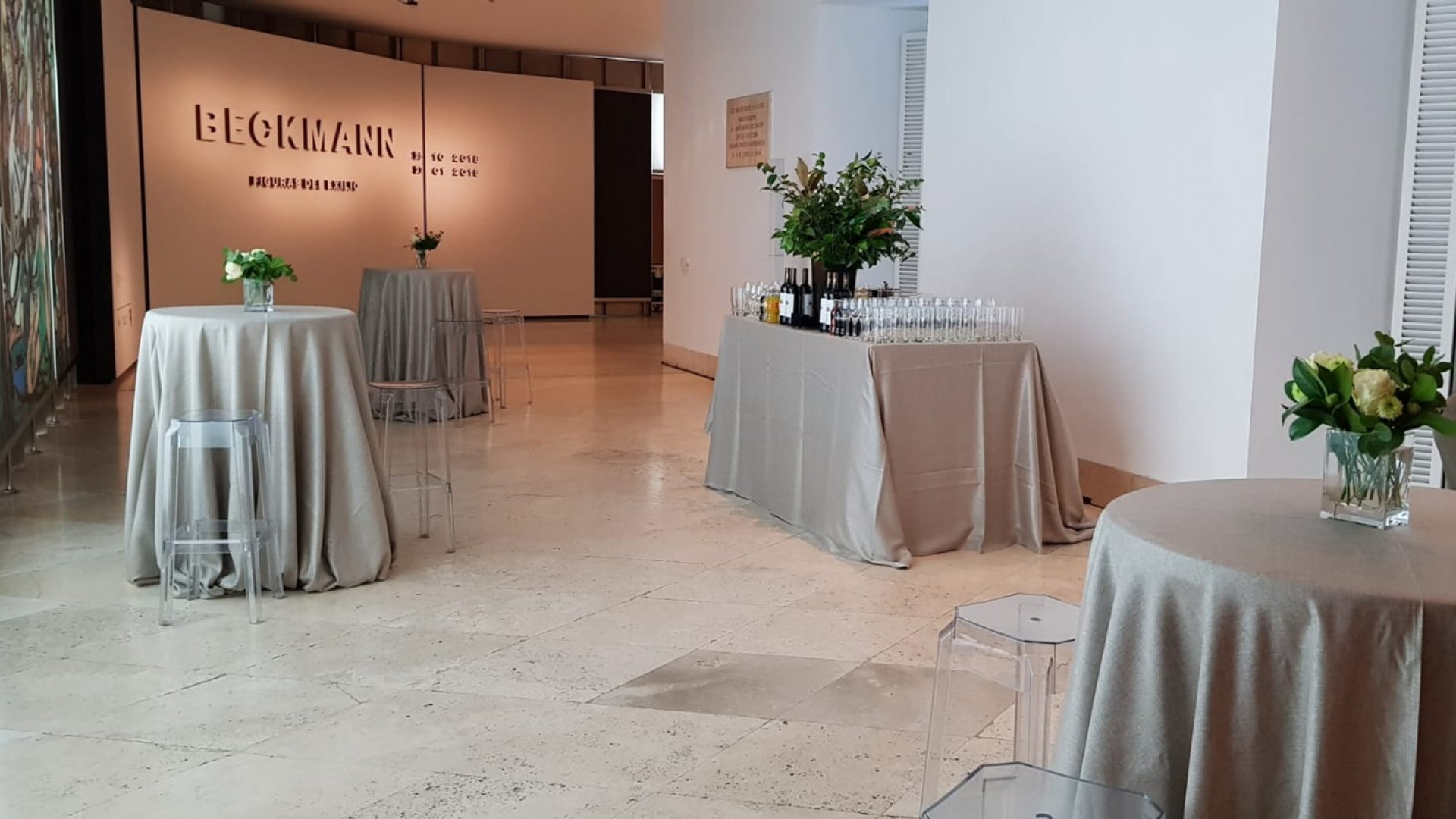 Varias mesas redondas con banquetas transparentes y manteles grises en la curva de las exposiciones temporales 