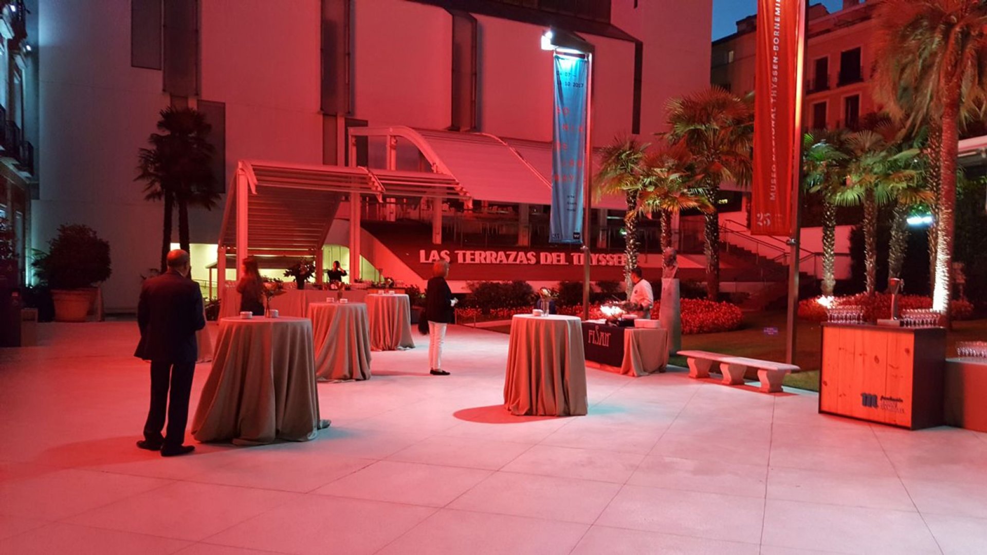 Jardín del museo con varias mesas redondas y decorado con un alumbrado en tonos rojizos