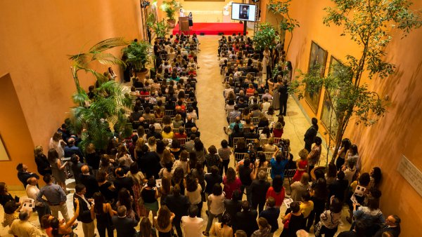 Evento lleno de gente en el hall central con un escenario rojo al fondo