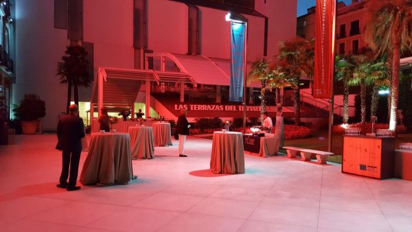 Jardín del museo con varias mesas redondas y decorado con un alumbrado en tonos rojizos