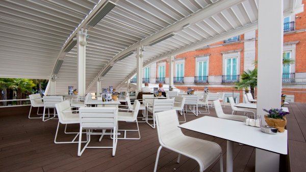 Varias mesas y sillas blancas en la terraza, el techo es de metal blanco